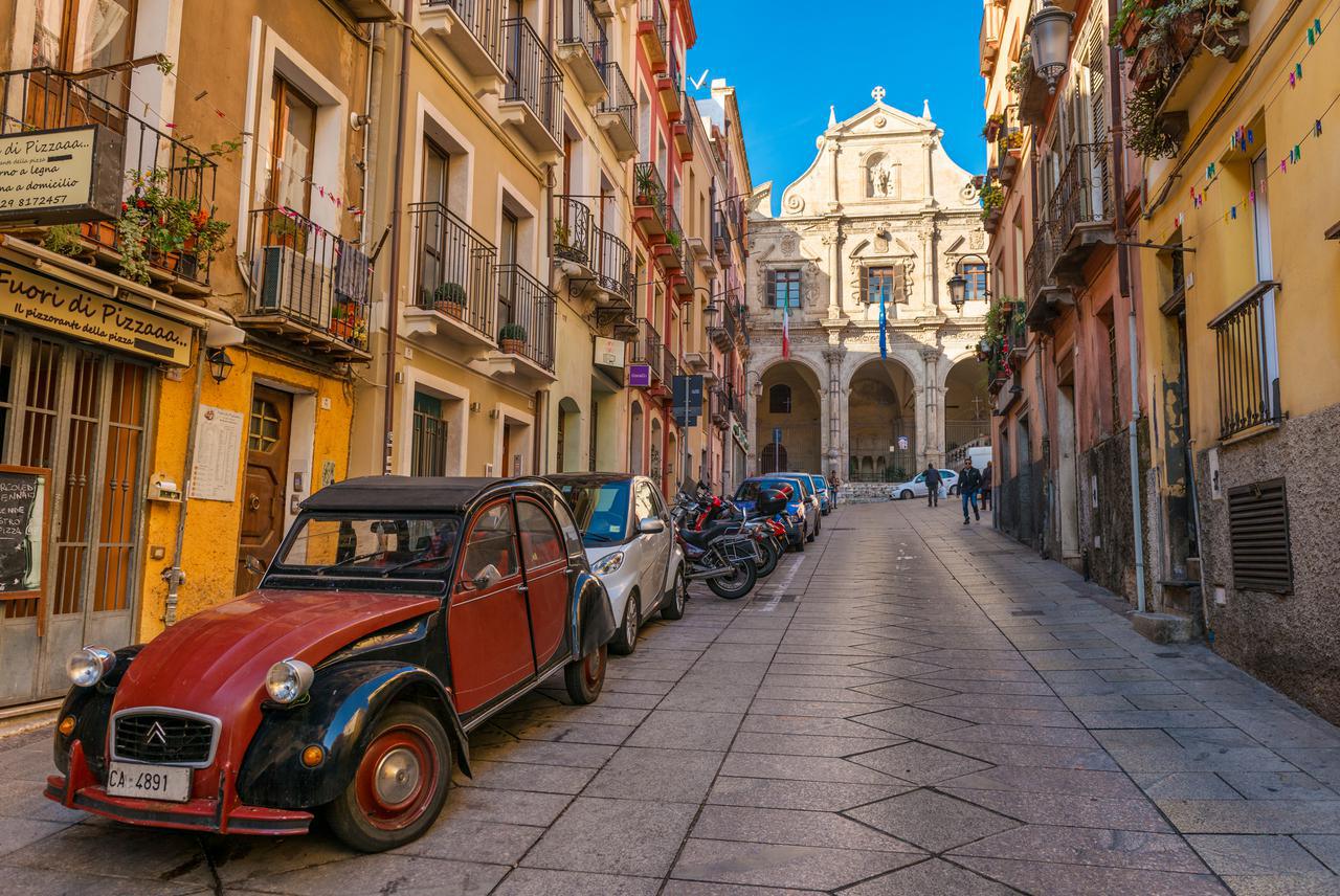 Vista della via con le vecchie case, la chiesa e la sagrestia del san Michele e l'automobile rossa d'annata sopra via Domenico Alberto Azuni