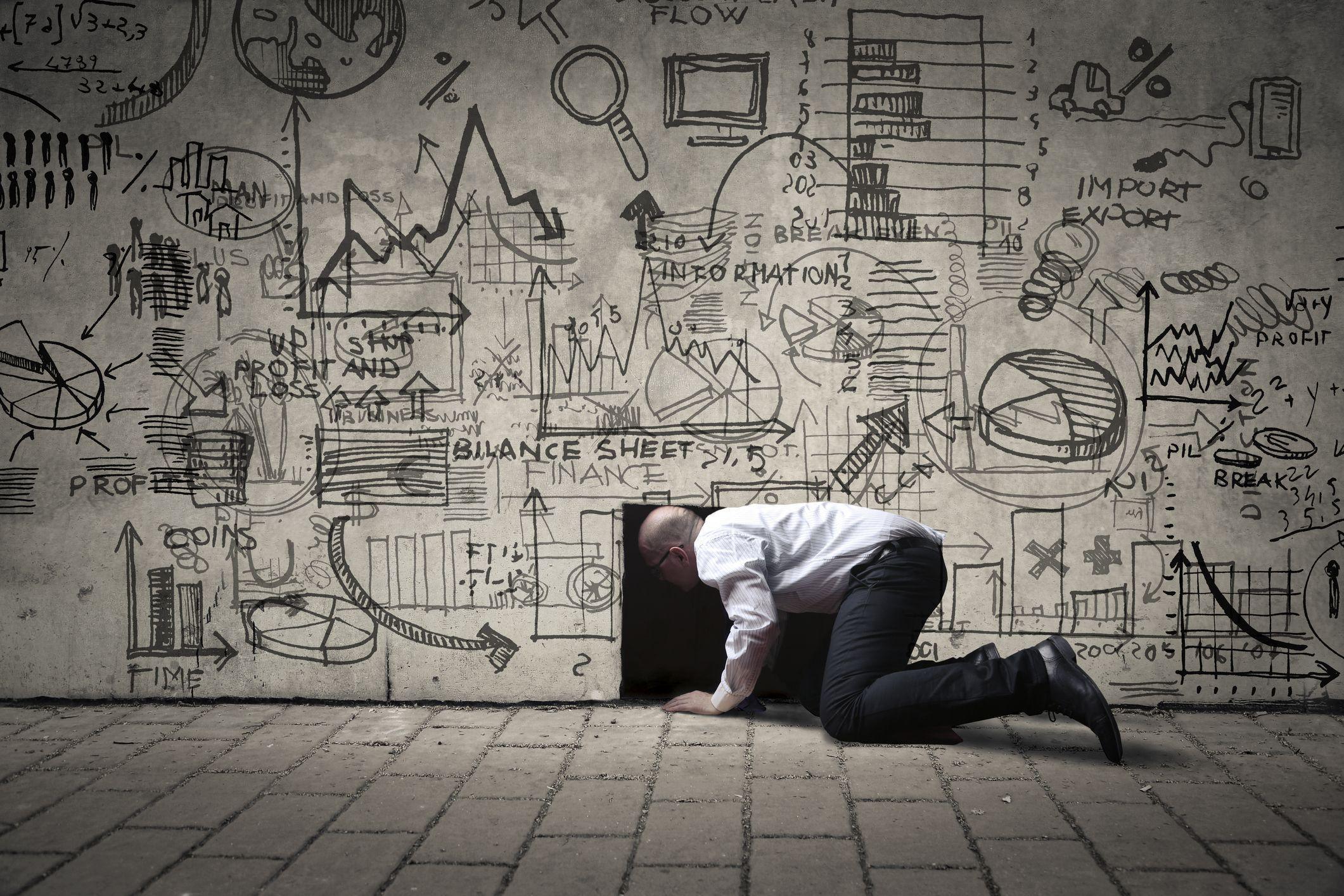 Homme d'affaires rampant dans un petit trou noir, avec des illustrations sur le mur. Photo : bowie15/iStock
