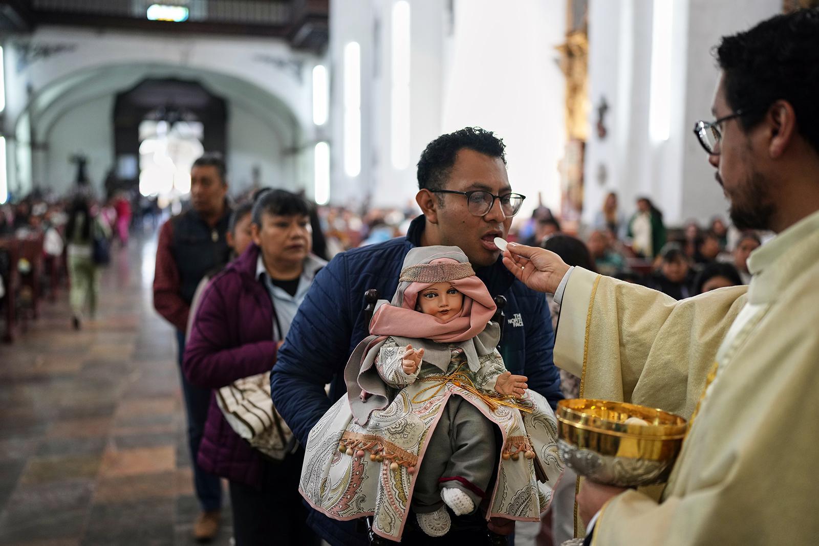 يتناول رجل القربان المقدس وهو يحمل تمثالاً صغيراً ليسوع الطفل خلال قداس عيد الشموع في الكنيسة الكاثوليكية في زوتشيميلكو، مدينة مكسيكو، يوم الاثنين 2 فبراير 2026. (صورة من وكالة أسوشييتد برس/إدواردو فيردوغو) 